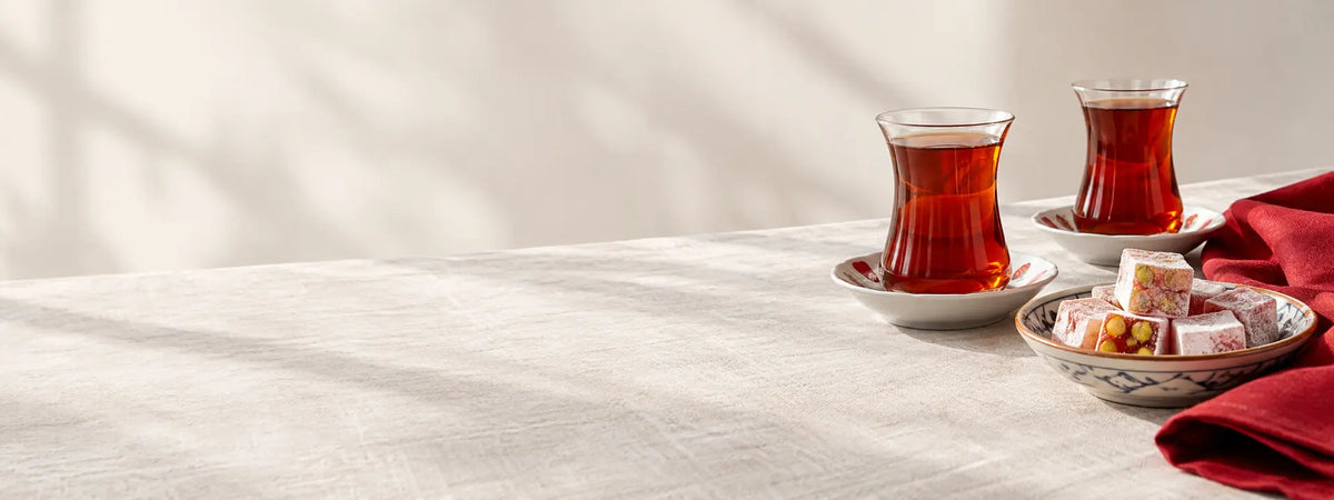 Two glasses of Turkish tea and a dish of lokum on a linen table beside a red cloth.