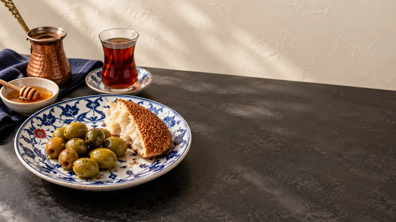 Olives and sesame bread on a blue and white plate with honey, tea and a copper cezve.