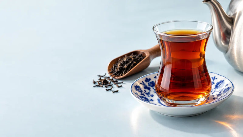 A glass of black tea on a blue and white saucer with loose tea leaves and a teapot.