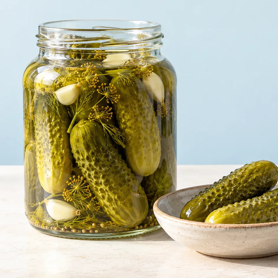 A glass jar of pickled cucumbers with dill and garlic, and a bowl of pickles.