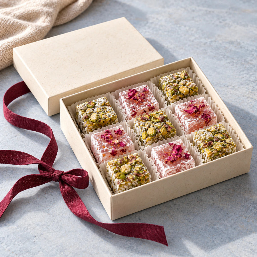 An open ivory gift box of assorted pistachio and rose Turkish delight with a burgundy ribbon.